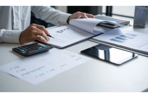 Person reviewing financial reports with calculator and tablet.