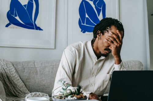 Man looking stressed at home, on laptop after forgetting to set a covid payment self assessment reminder