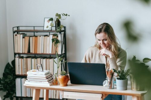 Smiling freelancer working on laptop against bookcase at home desk