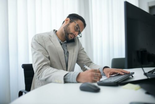 Man working at desk while on the phone, trying to sort out his tax audit in 2023